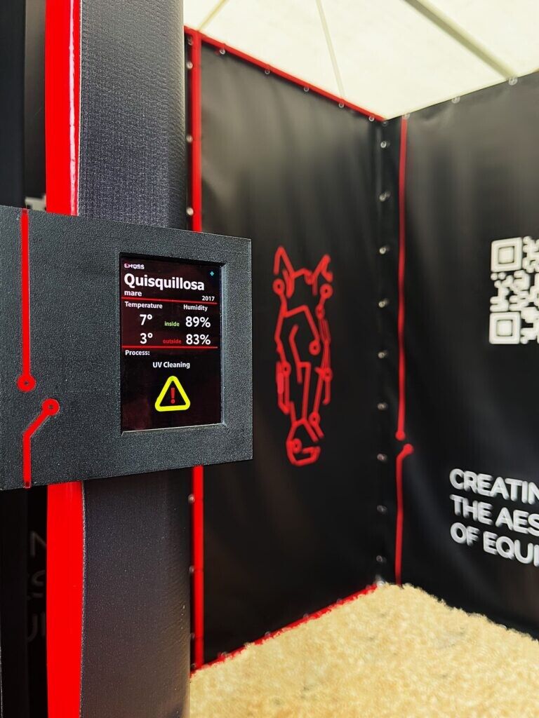 A panel on the stall frame reading the mare Quisquillosa's box — temperature and humidity inside against outside, and a UV cleaning cycle running