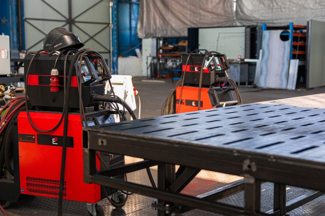 The welding table in the hall, a welding power source standing at the edge of its slotted top