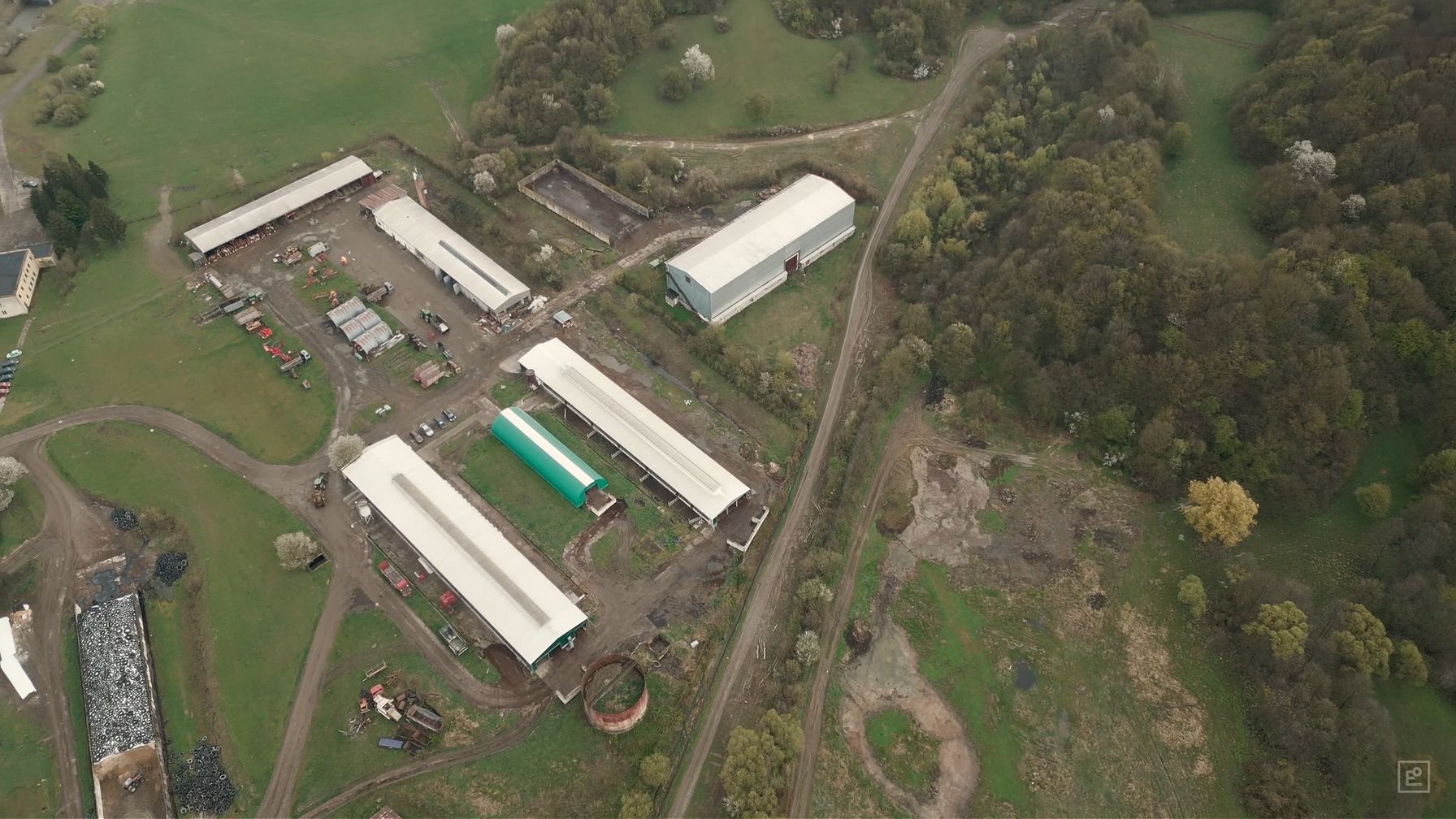 An aerial view of a livestock farm — long barns, a manure tank and silage stores between fields and woodland