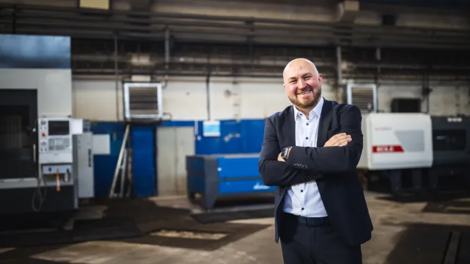 EHOSS founder Viktor Kvachan standing in the machine hall, arms folded, the CNC machines behind him