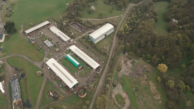 An aerial view of a livestock farm — long barns, a manure tank and silage stores between fields and woodland