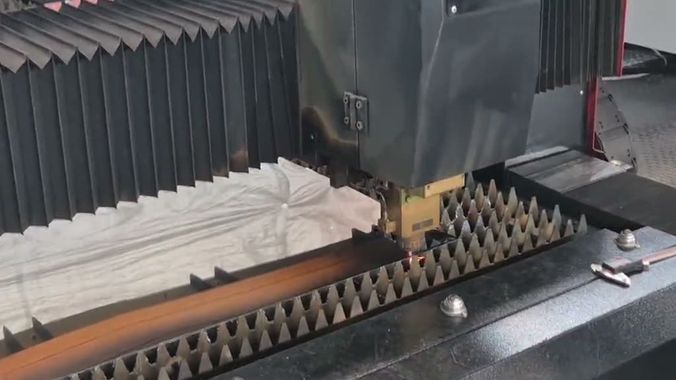 The fibre laser mid-cut, the head tracking a glowing kerf down a sheet lying on the slat bed